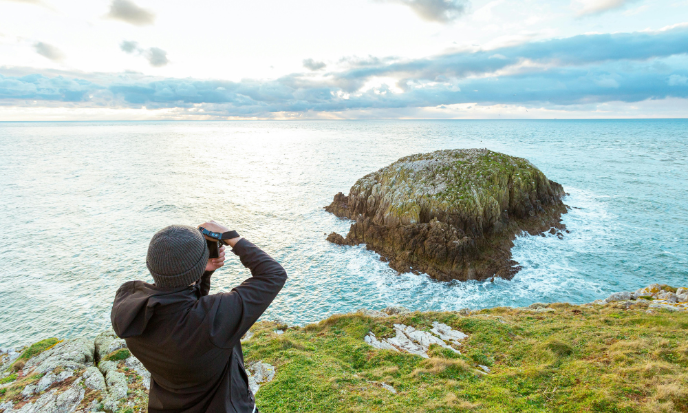 Back View of a Man Photographing a Rocky Island on the Coast of Anglesey, Wales